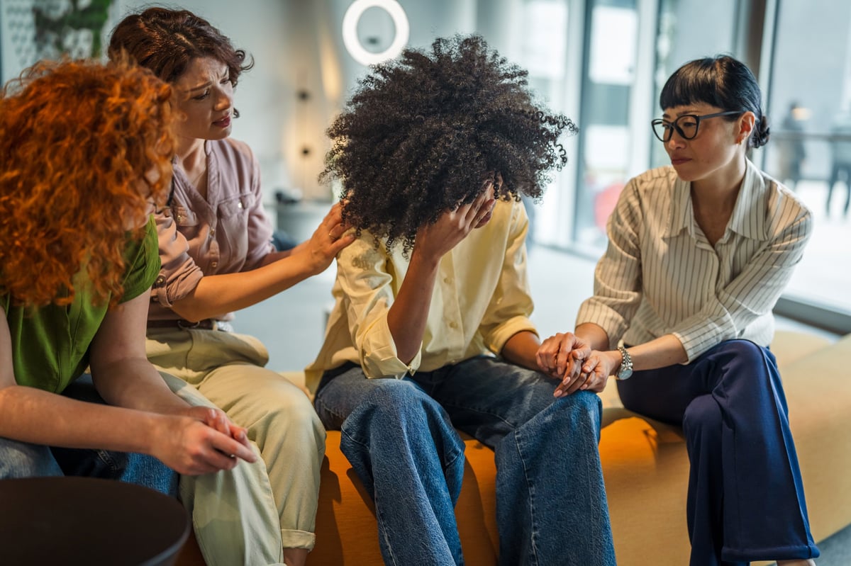 A diverse group of women holding hands and offering comfort to a friend during a supportive conversation