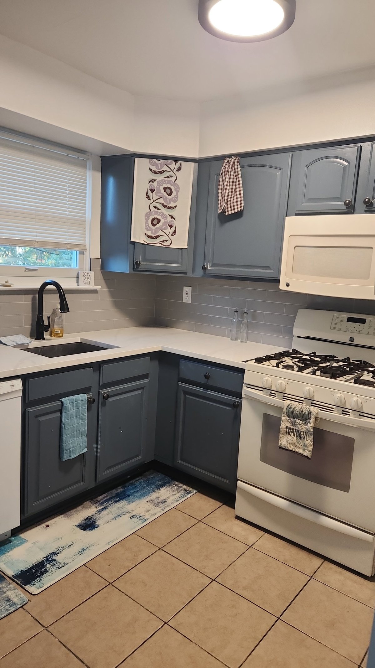 Modern kitchen with gray cabinets, white countertops, stainless steel appliances, subway tile backsplash, and beige tile flooring