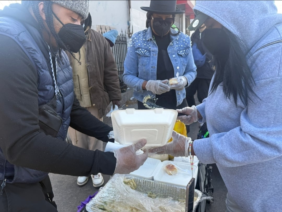 Group of people in winter clothing receiving food from a distribution table outdoors